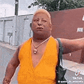 a man wearing a yellow tank top and a necklace is walking down a street .