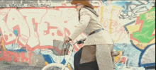 a woman is riding a bike in front of a wall with graffiti on it including the letters k and t.
