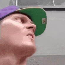 a man wearing a purple hat and a green hat is looking up at something .