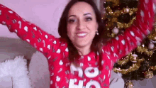 a woman in a red sweater is standing in front of a christmas tree with her arms in the air .