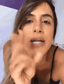a woman in a black tank top is pointing at the camera with her finger