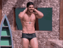 a shirtless man in swim trunks is standing in front of a rock wall