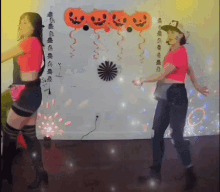 two women are dancing in front of a wall decorated with pumpkins and balloons