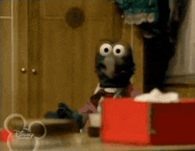 a disney puppet is sitting in front of a red box of tissues