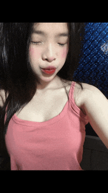 a girl in a pink tank top looks down with her eyes closed