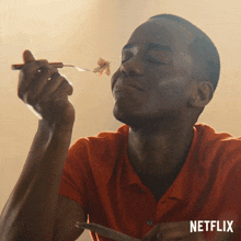 a man in an orange shirt is eating a piece of food with a netflix logo behind him