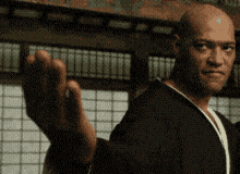 a bald man in a black robe is waving his hand in front of a window
