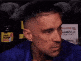 a man in a blue shirt is looking at the camera with a bottle of pre pump in the background