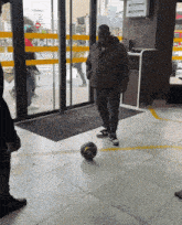 a man is kicking a soccer ball in front of a sliding glass door with a sign that says no smoking