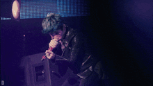 a man in a leather jacket singing into a microphone with the letter d in the corner