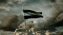 a flag on top of a rocky hill with clouds in the background