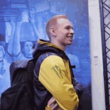 a man wearing a yellow monster sweatshirt stands in front of a large screen