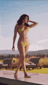 a woman in a yellow bikini is standing next to a swimming pool