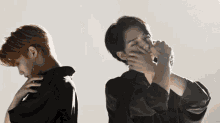 two men are standing next to each other and one is covering his face