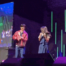 a man in a red jacket stands next to a woman in a blue dress on a stage holding a microphone