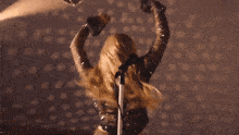 a blonde woman is singing into a microphone with her arms in the air