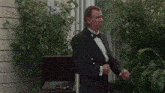 a man in a tuxedo stands in front of a plant