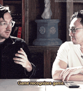 two men are sitting at a table with the words game recognizes game below them