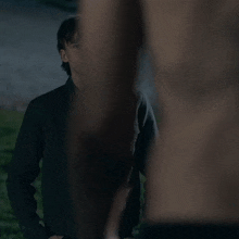 a young man in a black jacket stands in the grass