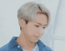 a young man with short blonde hair is wearing a blue striped shirt and a white t-shirt .