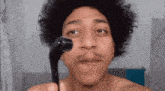 a shirtless man with curly hair is holding a derma roller to his face .
