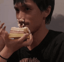 a man in a black shirt is eating a piece of cake with whipped cream on his nose