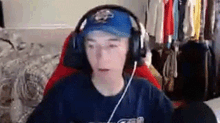 a young man wearing headphones and a baseball cap is sitting in a gaming chair .
