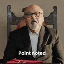 a man with glasses and a beard is sitting in a chair with the word point noted written below him
