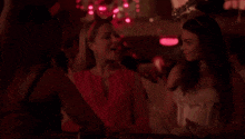two women are standing next to each other in a dark room with red lights . one of the women is wearing devil horns .