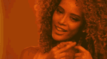 a woman with curly hair looks at the camera with a yellow background
