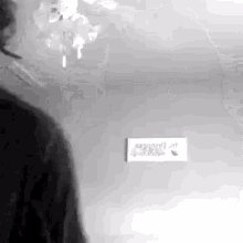 a black and white photo of a person standing next to a wall with a sign on it .