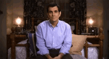 a man in a blue shirt is sitting on a bed with his legs crossed .