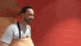 a man wearing an apron and a shirt that says ' chicago ' on it is standing in front of a red wall