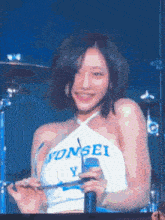 a woman is holding a microphone and smiling while wearing a white top that says yonsei on it .