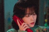 a woman wearing a green sweater is talking on a red telephone