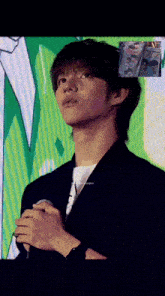 a young man in a suit is holding a microphone in front of a green background .