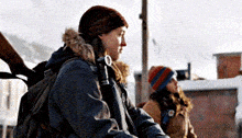 a woman with a backpack is standing next to another woman holding a gun
