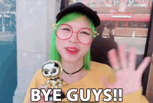 a woman with green hair and glasses holds a toy and says bye guys