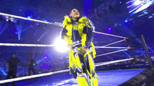 a wrestler is standing in a wrestling ring wearing a yellow and blue outfit .