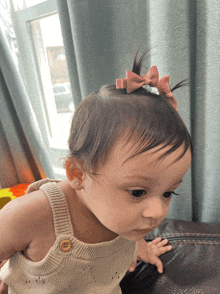 a baby with a pink bow in her hair is sitting on a couch