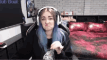 a girl with blue hair is wearing headphones and making a face in front of a sub goal sign