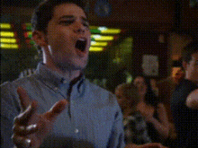 a man in a blue shirt is singing into a microphone with his arms outstretched