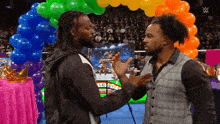 two men are standing next to each other in front of a rainbow of balloons in a wrestling ring .