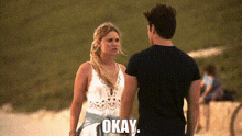 a man and a woman are standing next to each other on a beach and the man is saying okay .