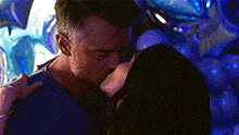 a man and woman are kissing in front of a bunch of blue balloons .
