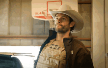a man wearing a cowboy hat and a ranger vest stands in front of a basketball hoop