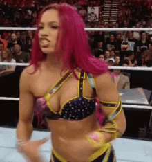 a female wrestler with pink hair is standing in a wrestling ring in front of a crowd .