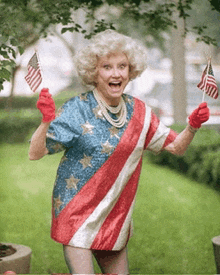 an elderly woman wearing a patriotic shirt is holding two american flags