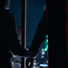 a man in a black jacket is opening a window at night .
