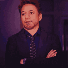 a man in a suit and tie has his arms crossed in front of a purple background